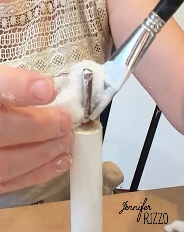 A person applies white paint to a small cylindrical object using a brush, with cotton in hand.