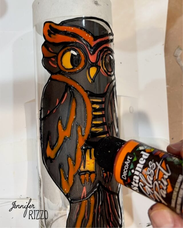 A hand applies orange glass paint to a black-outlined owl design on a vertical glass surface. The name Jennifer Rizzo appears in the bottom left corner.