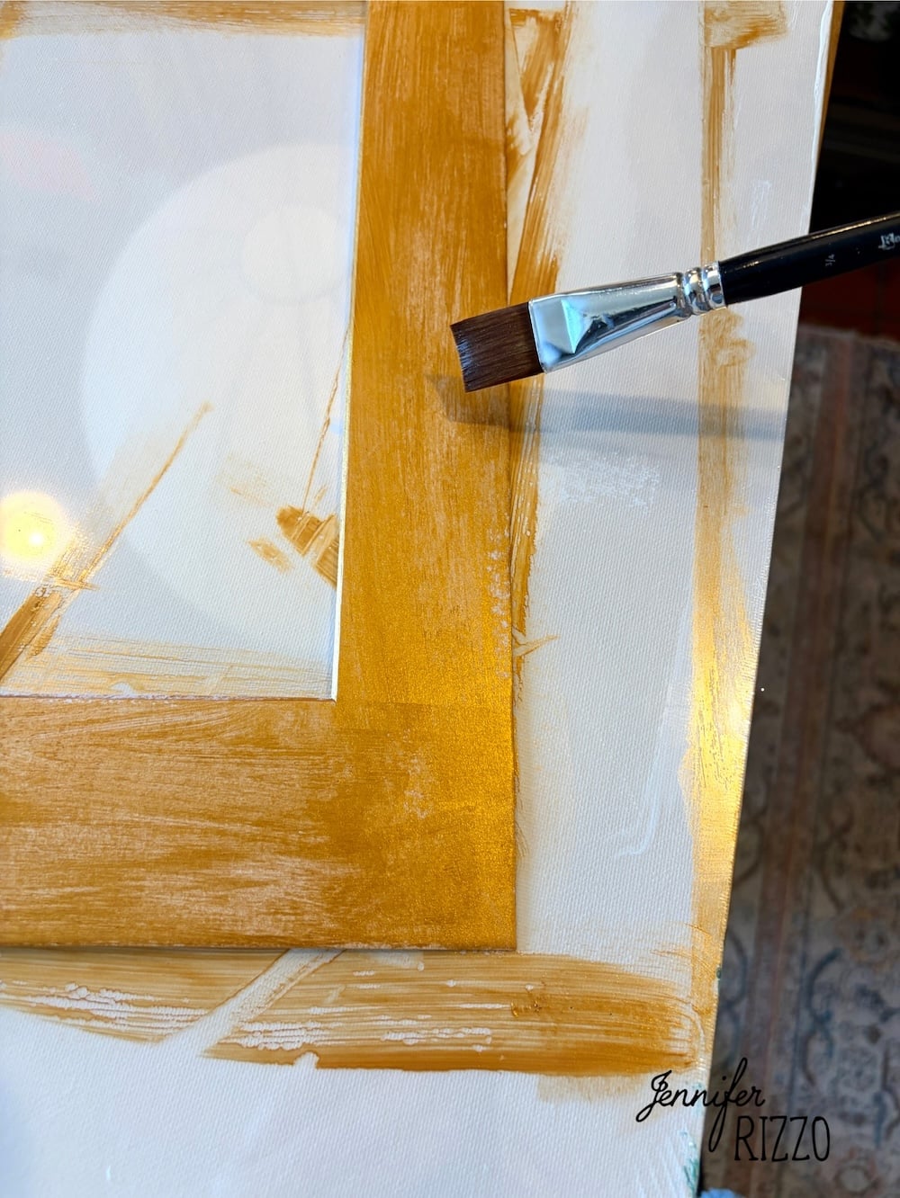 A paintbrush applies gold paint to the edge of a white canvas. The name “Jennifer Rizzo” appears in the bottom right corner.
