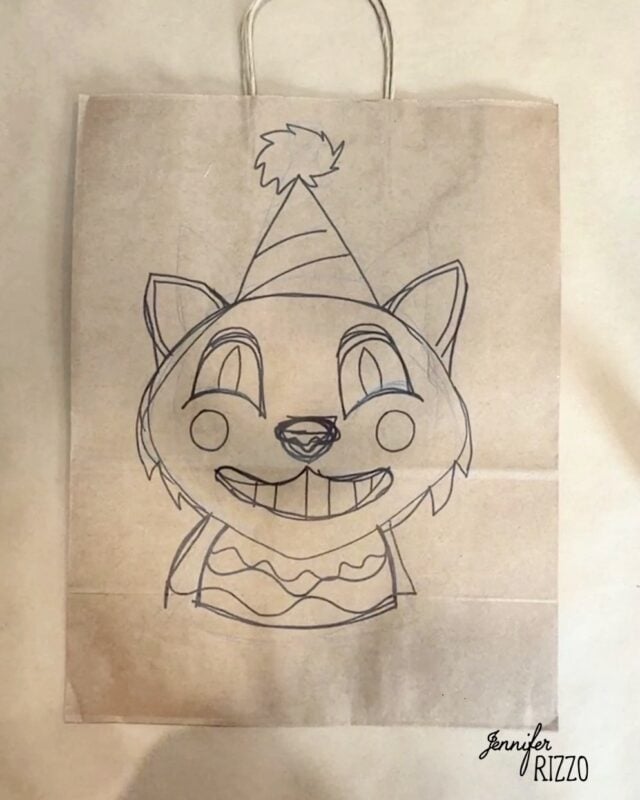 A paper bag features a hand-drawn cartoon cat wearing a party hat and sweater, smiling widely with big eyes and pointed ears.