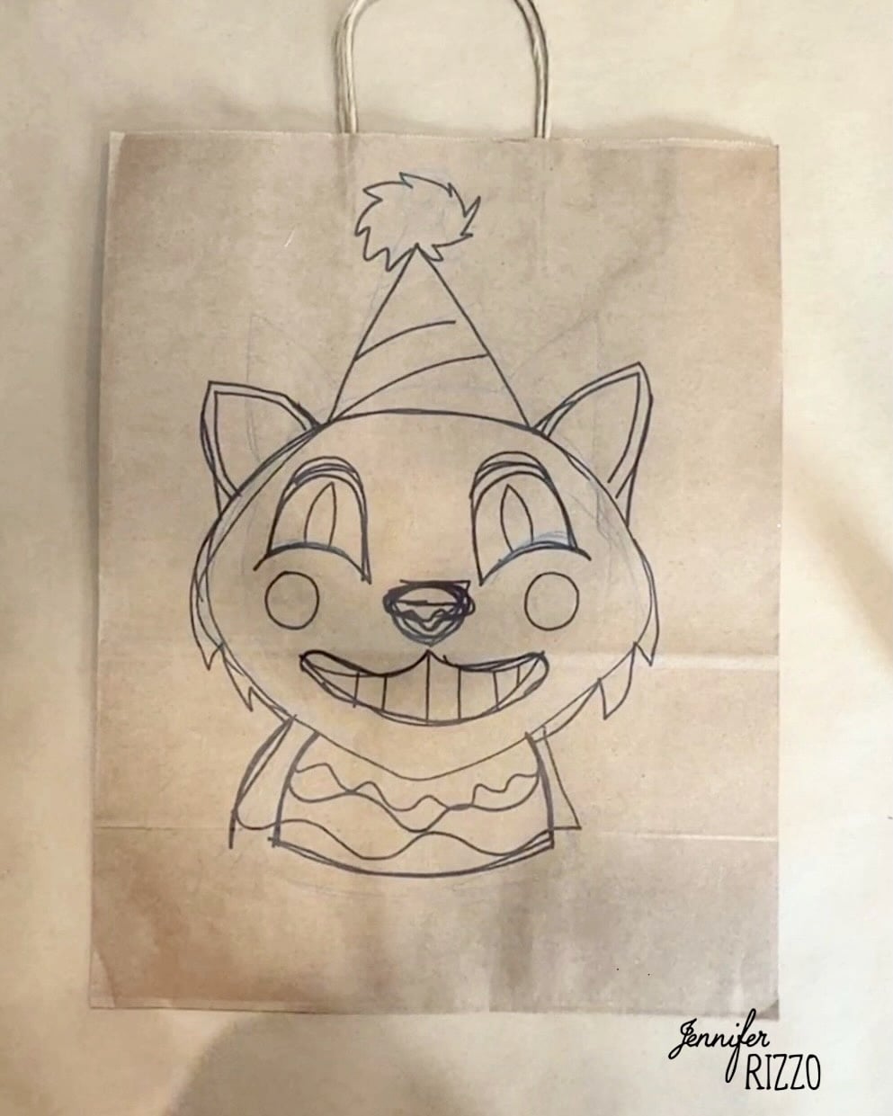 A paper bag features a hand-drawn cartoon cat wearing a party hat and sweater, smiling widely with big eyes and pointed ears.