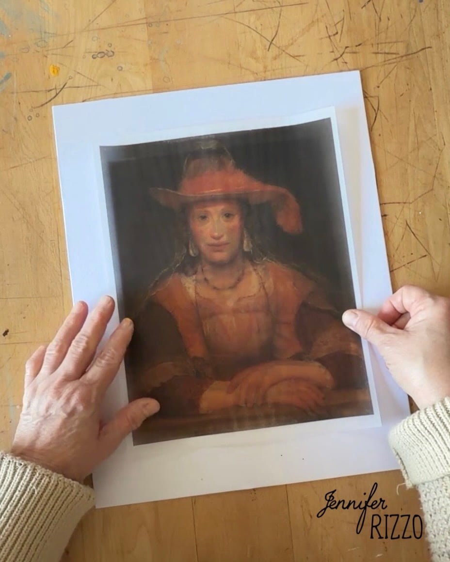Hands hold a printed portrait of a person in historical attire on a wooden table, with “Jennifer Rizzo” printed in the lower right corner.